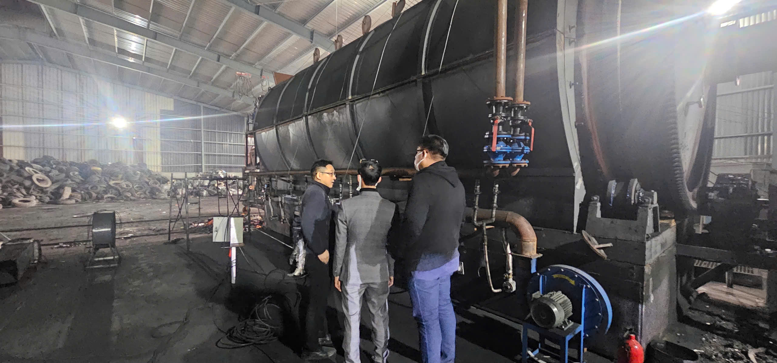 Industrial site with workers walking towards large structures under a blue sky with scattered clouds.